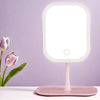 A pink LED desktop vanity mirror with adjustable lighting standing on a white surface.