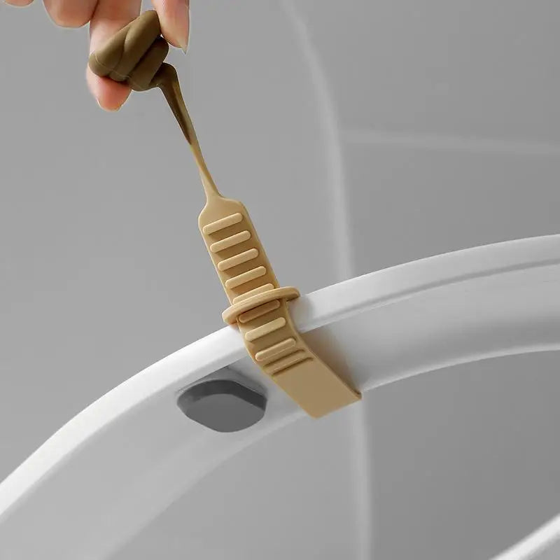 A hand is lifting a beige portable toilet lid lifter from a white toilet bowl.
