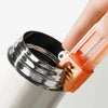 A hand is holding a cleaning brush set with a metal handle and an orange silicone brush head.