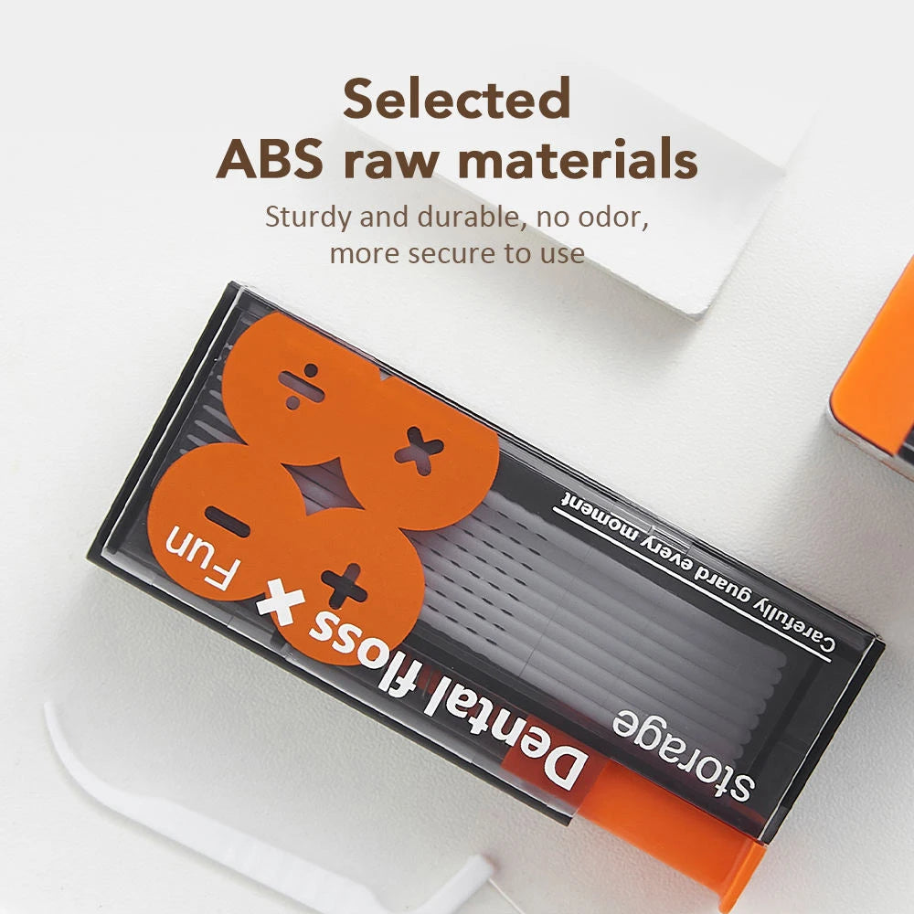 A black dental floss storage dispenser with an orange cap and clear floss visible on a white surface.
