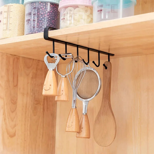 A black metal storage rack hanging on a wooden shelf, holding various kitchen utensils like whisks and spatulas.