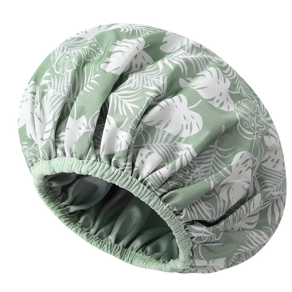 A reusable satin-lined shower cap in a green and white tropical leaf pattern.