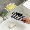 A hand is placing a light-colored soap bar onto a black wall mounted soap dish rack in a bathroom setting.