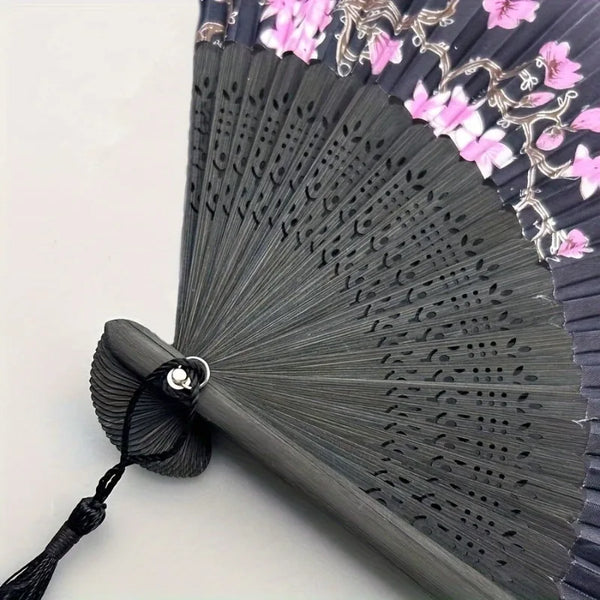 A close-up of a vintage floral cherry blossom hand fan with dark gray feathers and pink blossoms.