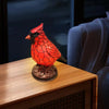 A vibrant orange resin bird sculpture sits on a wooden table next to a gray fabric chair.