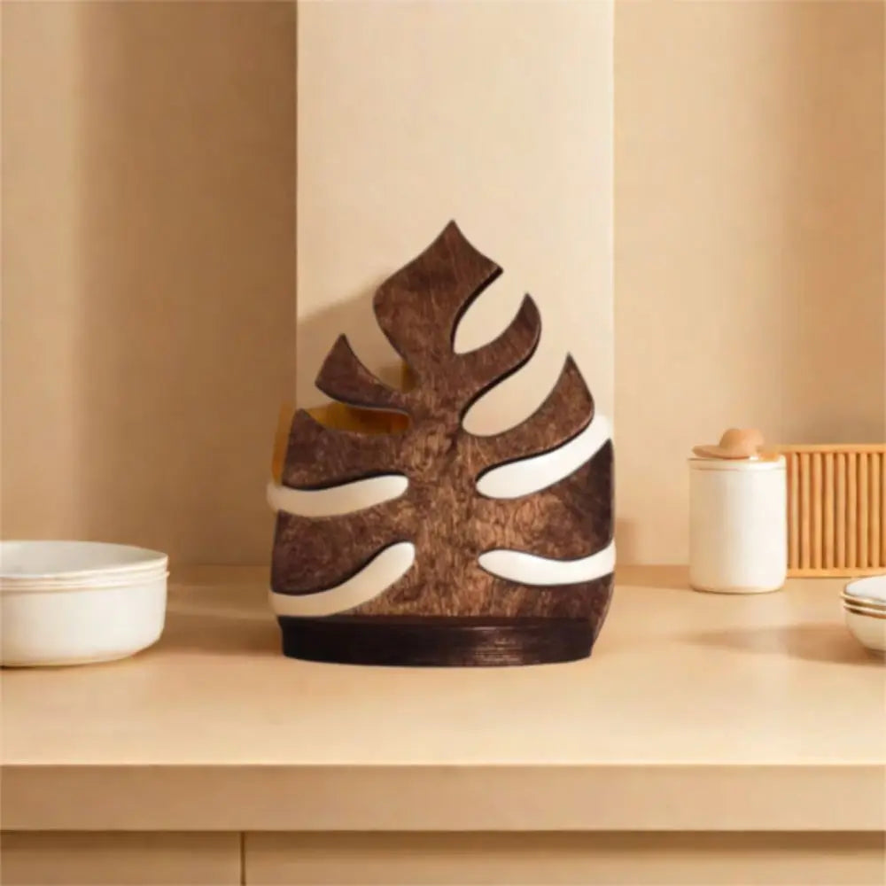 A decorative wooden wall art frame shaped like a leaf in brown and white tones displayed on a light wooden surface.