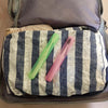 A light purple toothbrush is placed on a striped fabric inside a gray travel storage case.