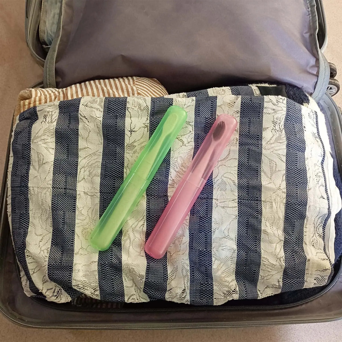 A light purple toothbrush is placed on a striped fabric inside a gray travel storage case.