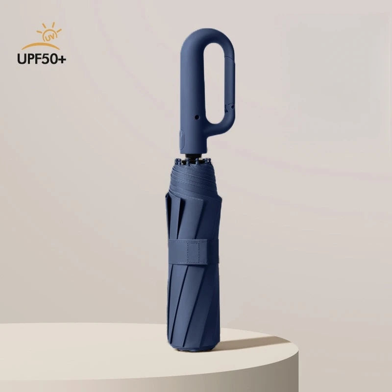 A dark blue windproof automatic folding umbrella standing upright on a light surface.