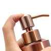 Eine Hand hält eine Flüssigseif-Dispenserflasche aus roségoldenem Edelstahl.