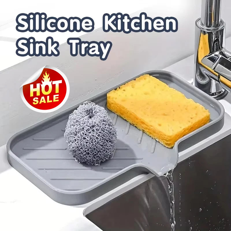 A silicone kitchen sink tray holding a yellow baked item and a scouring pad being rinsed under water.