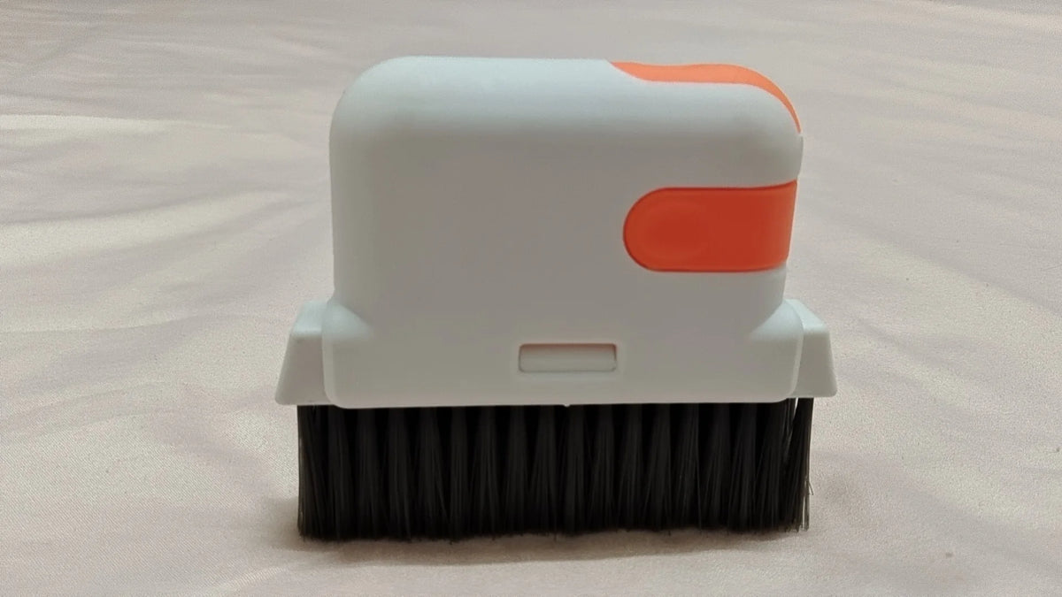 Una brocha de limpieza blanca con un acento naranja, mostrada contra un fondo claro.