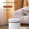 A white touchless sensor trash can is placed on a light-colored rug in a modern living room setting.