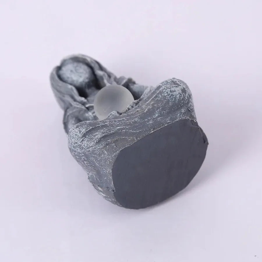 A gray resin statue of a moon goddess head with a smooth, spherical element.