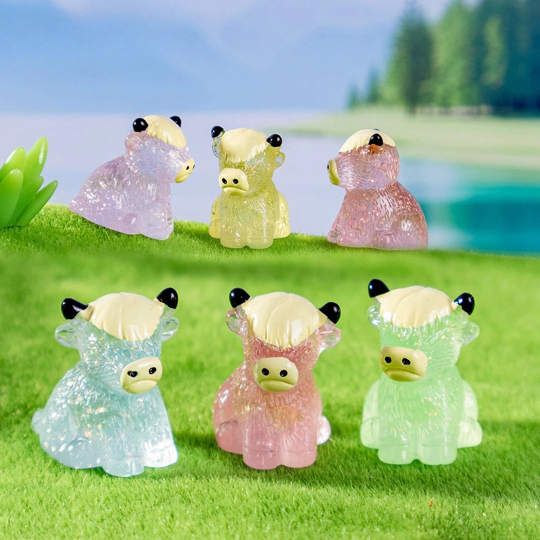A set of resin highland cow figurines in various colors, including pink, yellow, and green, displayed on bright green grass.