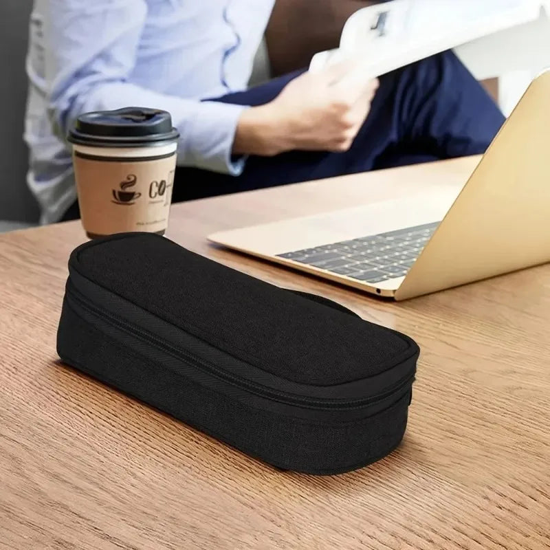A black multi-purpose travel electronics organizer bag resting on a wooden desk next to a laptop and a coffee cup.