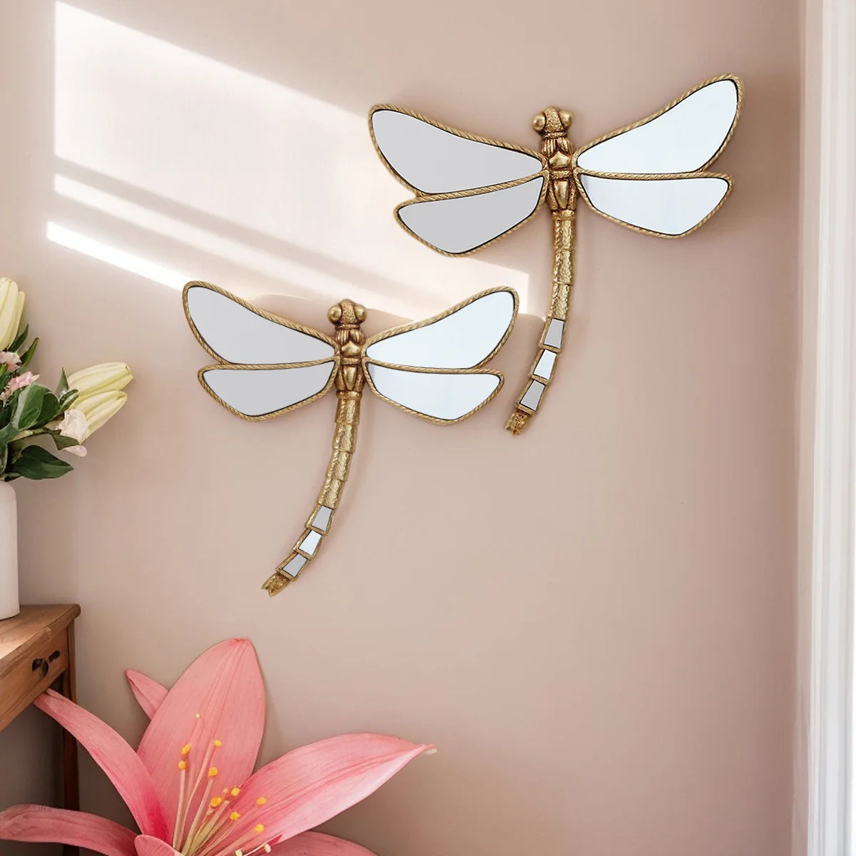 Golden dragonfly mirror wall decor featuring a gilded frame and white wings mounted on a beige wall.