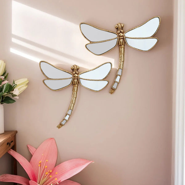 Golden dragonfly mirror wall decor featuring a gilded frame and white wings mounted on a beige wall.