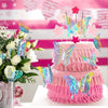 A pink tiered cake decorated with edible butterfly toppers and surrounded by white roses.