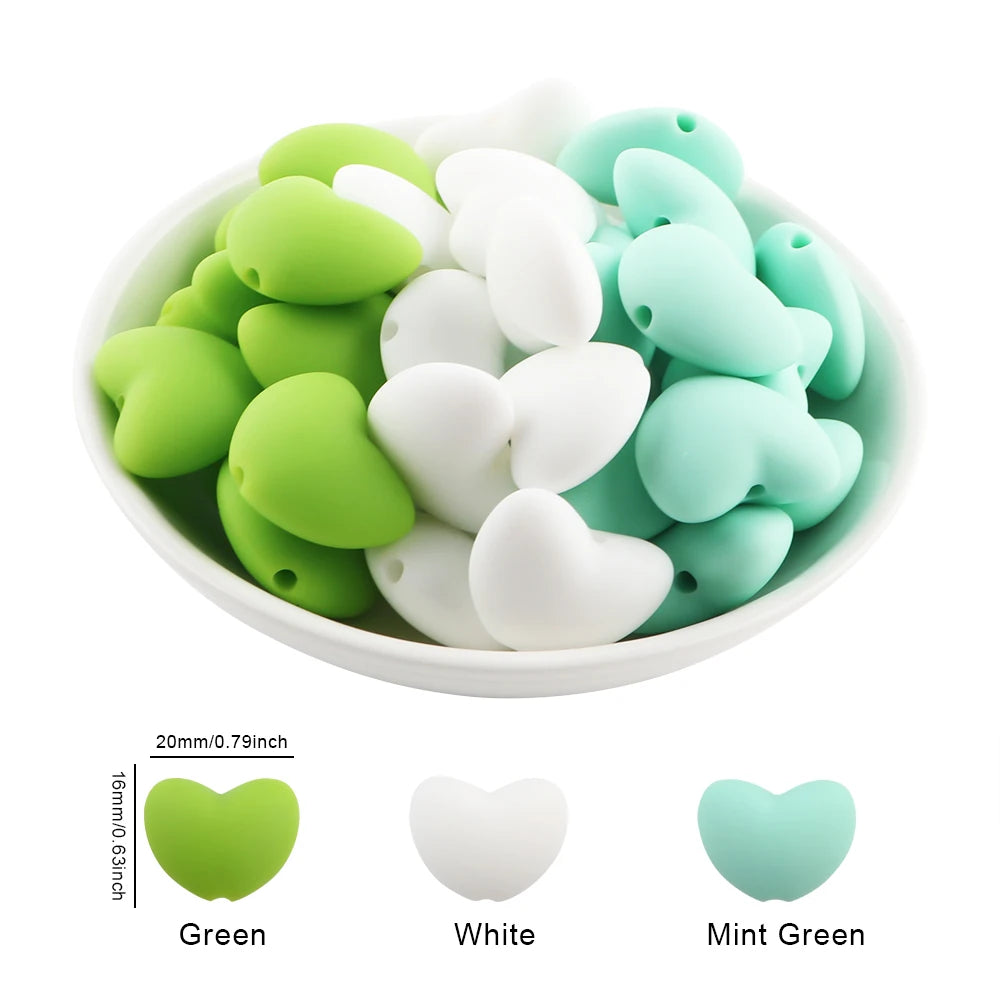 A bowl filled with ten silicone heart-shaped charm beads in green, white, and mint green colors.
