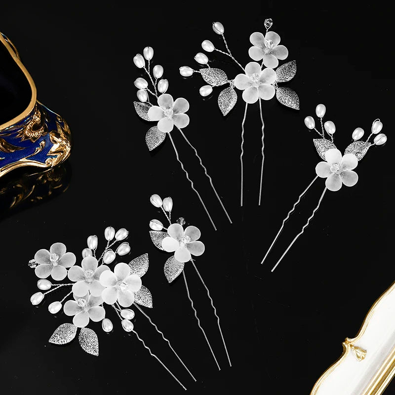 A set of delicate white pearl flower bridal hair clips with silver accents displayed on a black background.