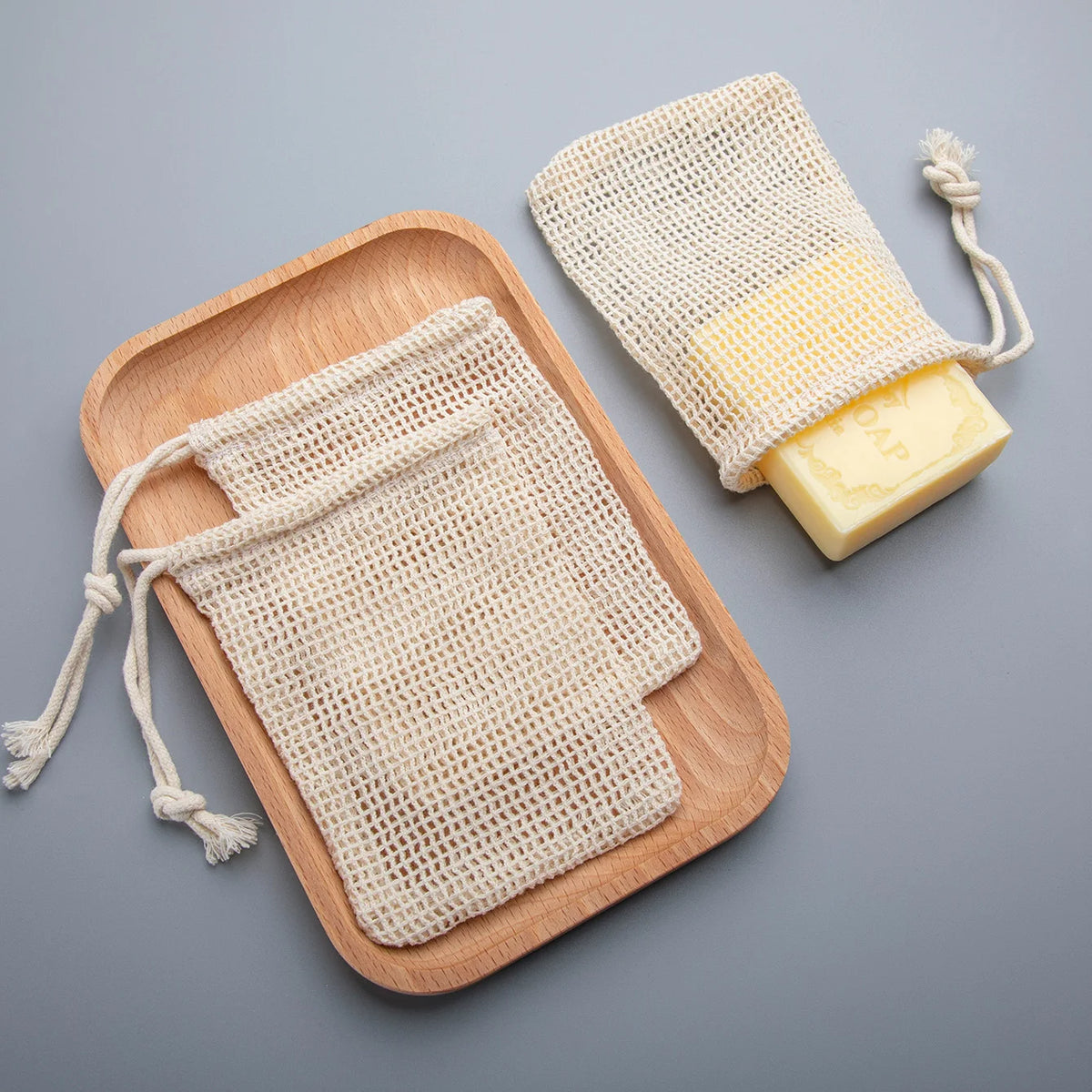 A set of natural cotton mesh pouches used to save soap, with a yellow bar of soap visible.