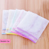A stack of translucent white, pink, and yellow heat resistant ironing cloths or press guards on a wooden surface.
