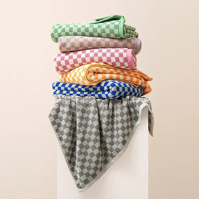 A stack of plaid cotton bath towels in various colors including green, purple, pink, yellow, and blue.