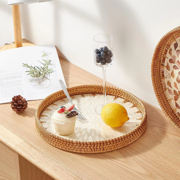 A round rattan serving tray with mother of pearl inlay holds a lemon, blueberries, and a small dessert.