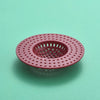 A round, pink plastic kitchen sink drain strainer with a grid pattern for catching hair and debris.