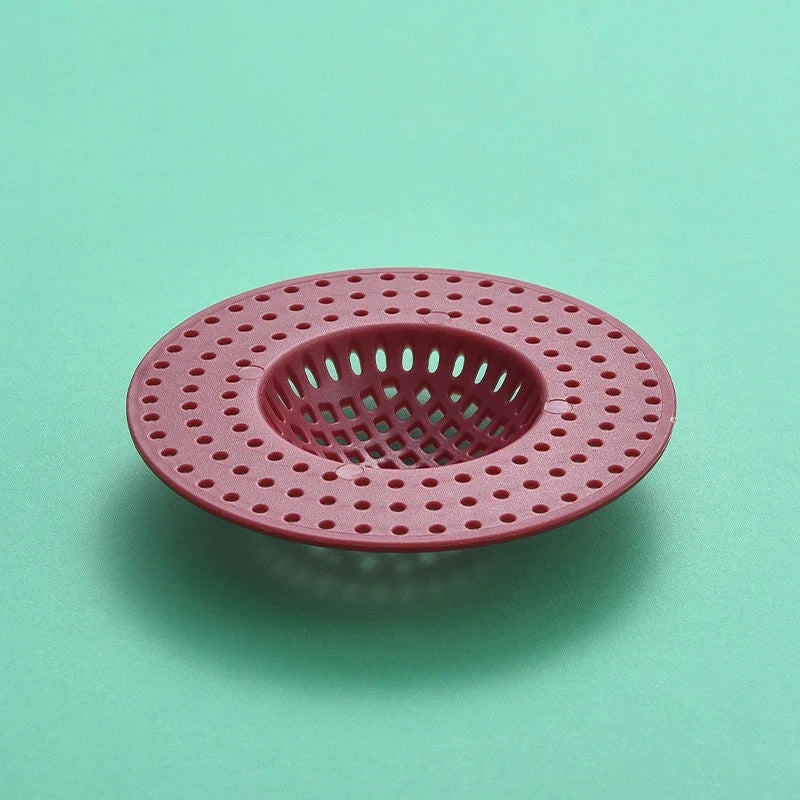 A round, pink plastic kitchen sink drain strainer with a grid pattern for catching hair and debris.
