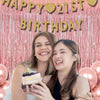 Two young women smiling in front of a pink glitter tinsel curtain backdrop for a birthday celebration
