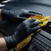 A hand wearing a black nitrile glove is holding a yellow cleaning cloth over an electronic device.