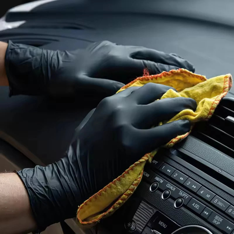 A hand wearing a black nitrile glove is holding a yellow cleaning cloth over an electronic device.