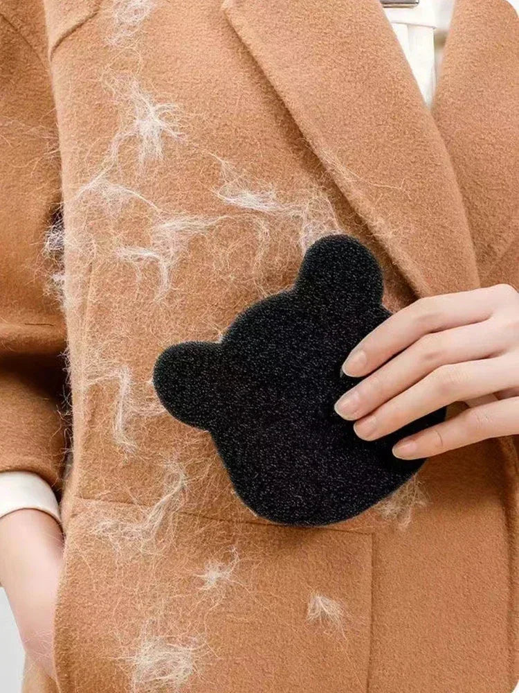 A hand holds a black pet hair remover sponge against a brown coat fabric.