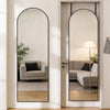 A full body wall mirror with an arched top and thin aluminum frame reflecting a modern living room interior.