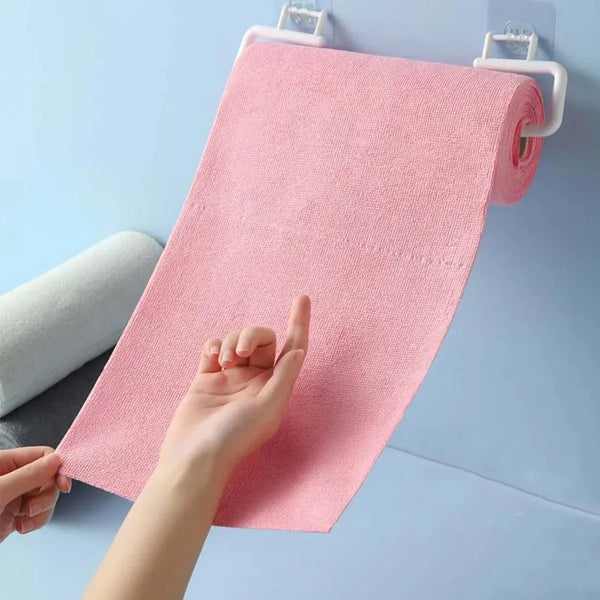 A hand is pulling a pink microfiber tear-off cleaning cloth roll from a hanger against a light blue background.
