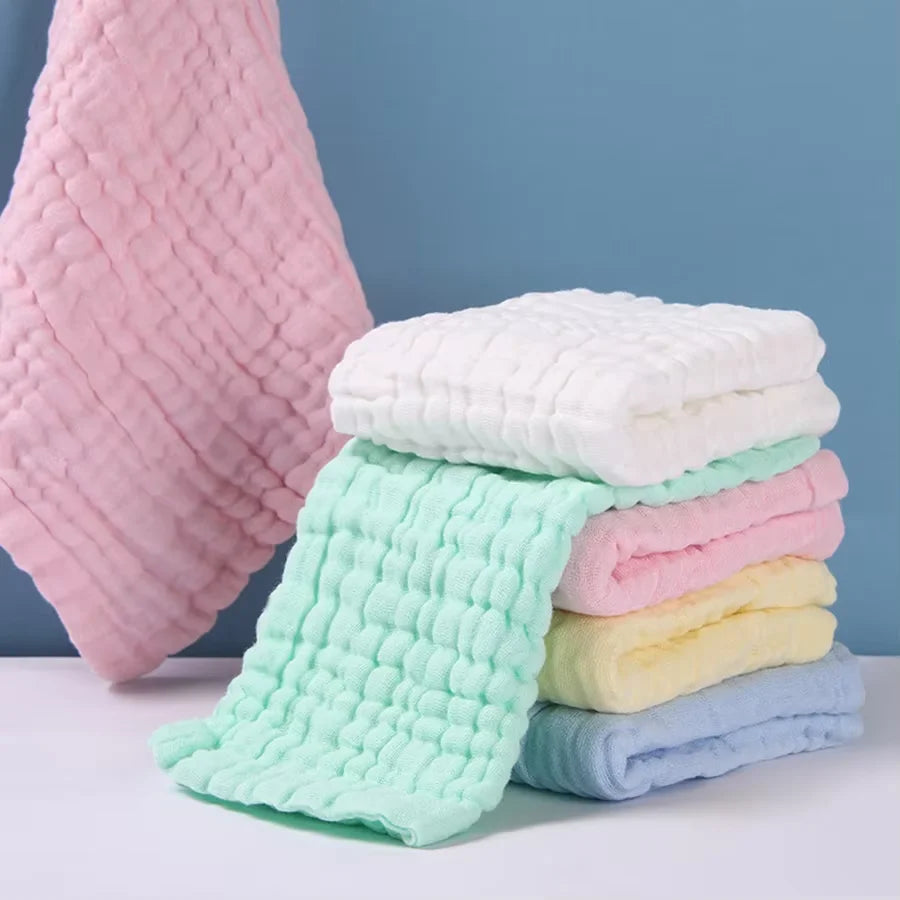 Una pila de cinco toallitas húmedas orgánicas para bebé y cara de algodón en rosa, verde y blanco sobre una superficie blanca