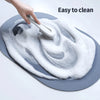 A hand is cleaning a gray bath mat with a white brush, demonstrating its easy to clean feature.