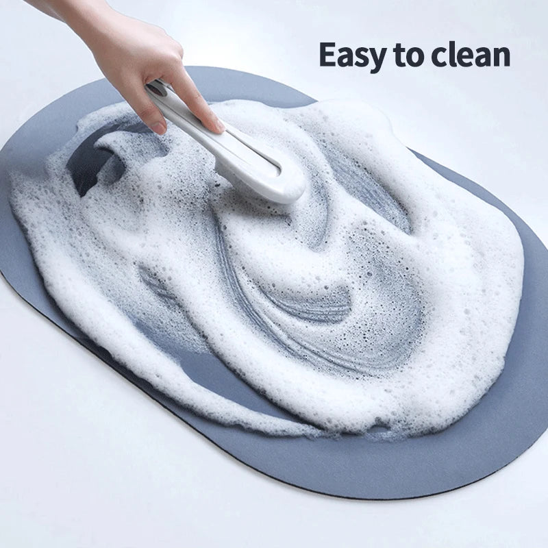 A hand is cleaning a gray bath mat with a white brush, demonstrating its easy to clean feature.