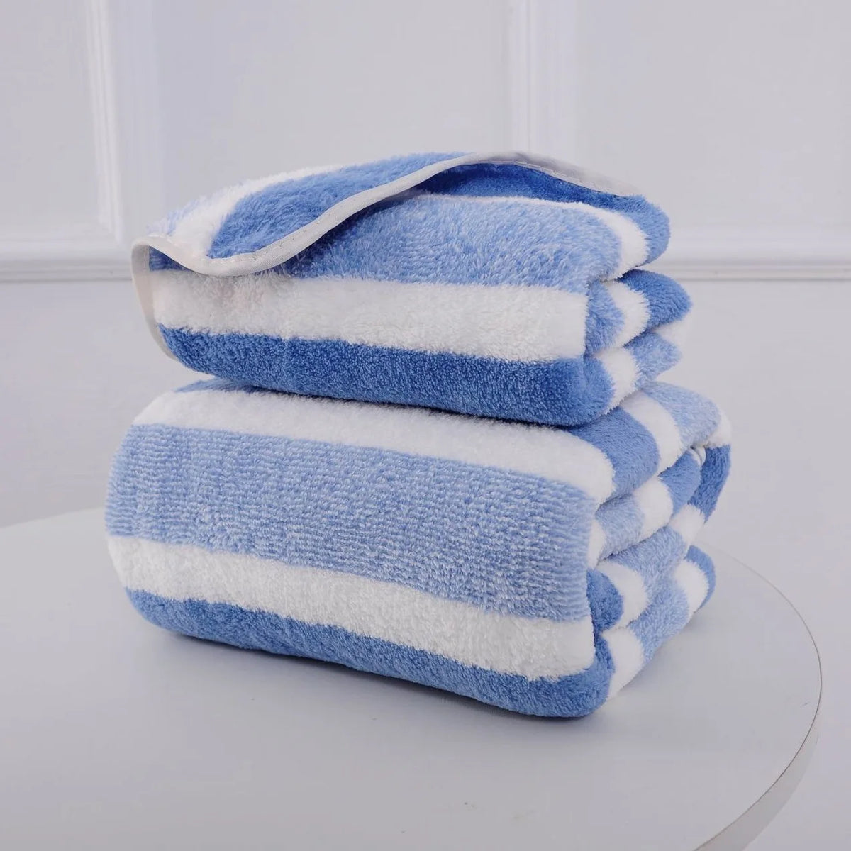 Ein Stapel blau-weißer gestreifter Mikrofaserhandtücher, ordentlich gefaltet auf einer weißen Oberfläche.