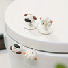 A white toilet seat with decorative lifter handles shaped like cartoon sheep and cows.