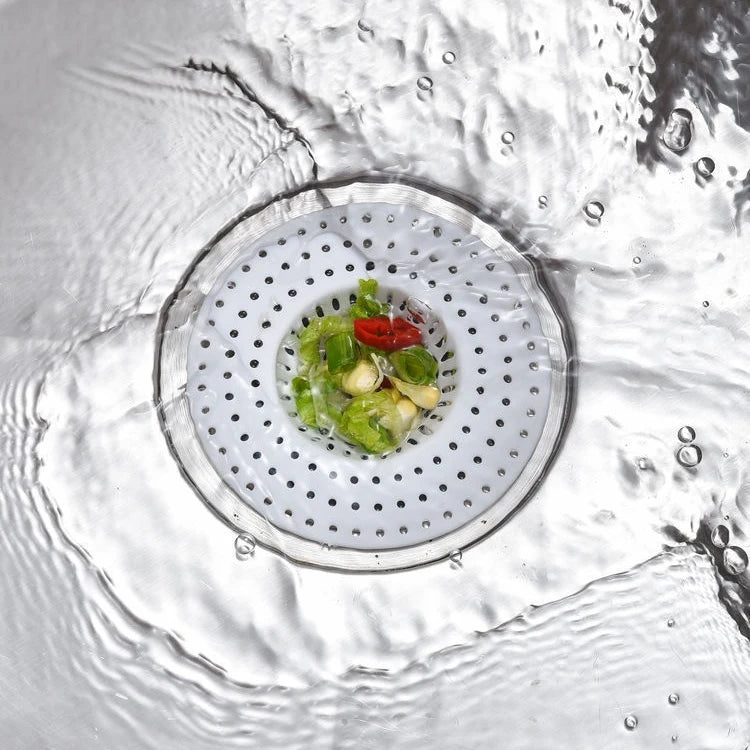 A close-up view of a kitchen sink drain strainer and hair catcher with green and red food scraps inside.