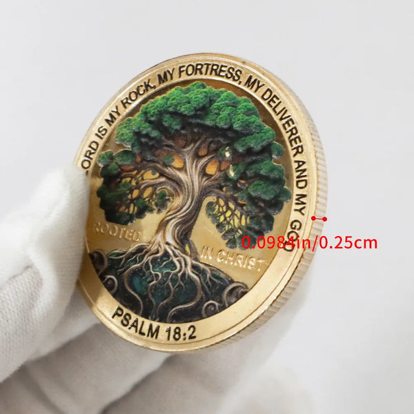 A gold coin featuring a tree design and scripture text, held in a hand.