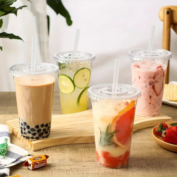 A glass of iced fruit smoothie in a clear plastic cup with a lid, served on a wooden board.