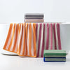 A set of plaid cotton bath towels in various stripes and solid colors stacked on a white surface.
