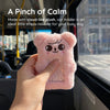 A pink plush doll shaped like a bear is held in a hand against a blurred background of a train window.