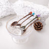 A glass filled with ice and several natural crystal spoons with colored crystals resting on a white surface.
