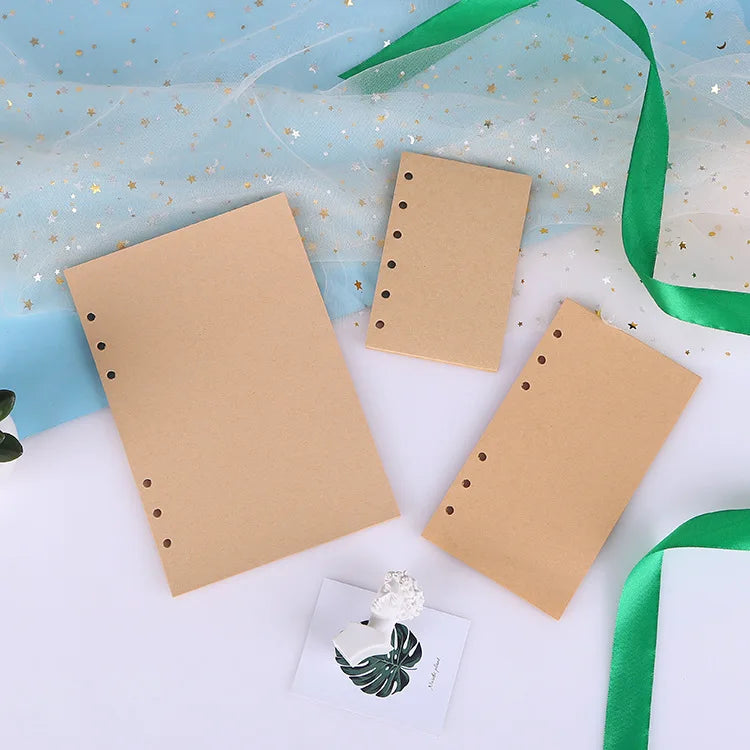 A set of blank kraft paper notebook refills with gold star accents and a green ribbon on a white background.