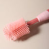 A pink silicone baby bottle cleaning brush with a pink handle is shown against a light background.